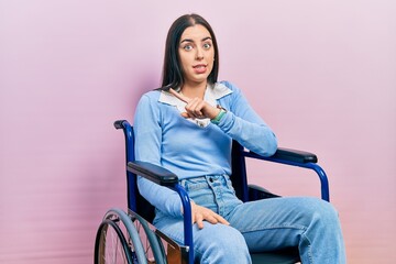 Beautiful woman with blue eyes sitting on wheelchair pointing aside worried and nervous with...