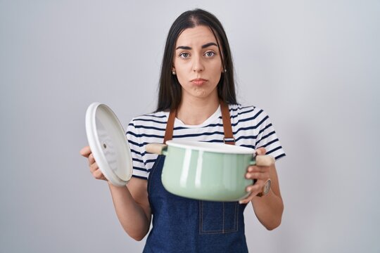 Young brunette woman wearing apron holding cooking pot depressed and worry for distress, crying angry and afraid. sad expression.