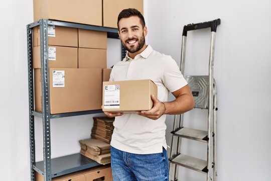 Young hispanic man smiling confident holding package at storehouse