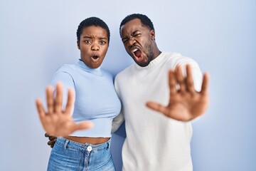 Young african american couple standing over blue background doing stop gesture with hands palms,...