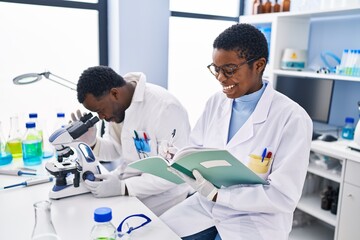 Man and woman scientists using microscope writing on notebook at laboratory