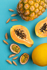 Ripe cut papaya, pineapple, melon, passion fruit, almonds on blue pastel background. Top view, close up.