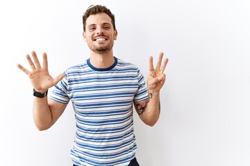 Handsome young man standing over isolated background showing and pointing up with fingers number eight while smiling confident and happy.