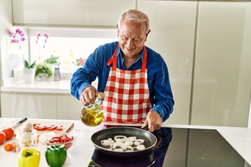 Senior man smiling confident pouring oil on frying pan at kitchen