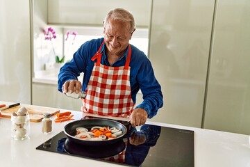 Senior man smiling confident pouring salt on frying pan at kitchen