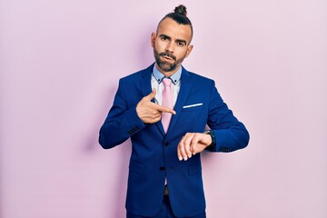 Young hispanic man wearing business suit and tie in hurry pointing to watch time, impatience, upset...