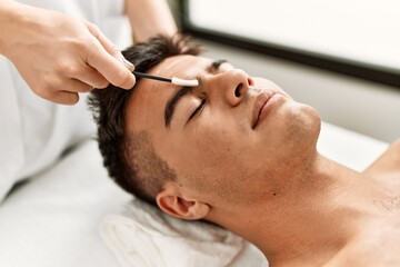 Young hispanic man relaxed having eyebrows treatment at beauty center