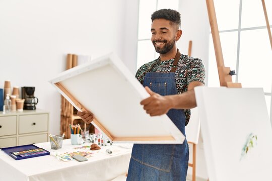 Young african american artist man smiling happy holding canvas at art studio.
