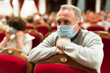 mature man in antivirus mask in theater watching a performance