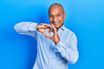 Middle age latin man wearing casual clothes and glasses smiling in love doing heart symbol shape with hands. romantic concept.