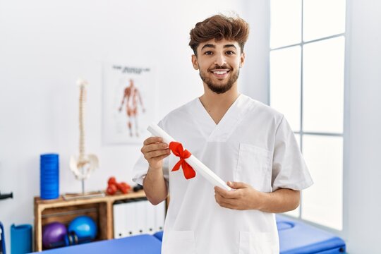 Young arab man wearing physiotherapist uniform holding diploma at clinic