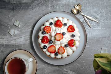 Top view on sweet creamy cake with berries and tea on grey background