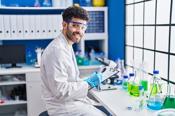 Young arab man wearing scientist uniform writing on clipboard at laboratory