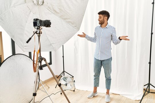 Arab young man posing as model at photography studio smiling showing both hands open palms, presenting and advertising comparison and balance