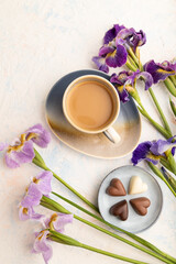 Cup of cioffee with chocolate candies and lilac iris flowers on white concrete background. top view, close up.