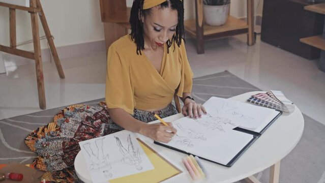High angle shot of female designer drawing fashion illustrations at coffee table while sitting on floor at home