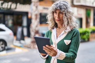 Middle age woman smiling confident using touchpad at street