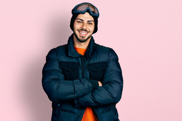 Young hispanic man with beard wearing snow wear and sky glasses happy face smiling with crossed arms looking at the camera. positive person.