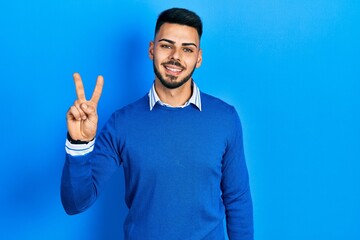 Fototapeta premium Young hispanic man with beard wearing casual blue sweater showing and pointing up with fingers number two while smiling confident and happy.
