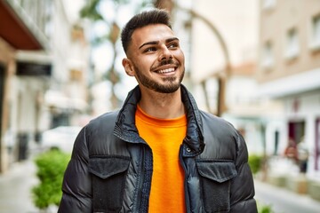 Fototapeta premium Handsome hispanic man with beard smiling happy and confident at the city wearing winter coat