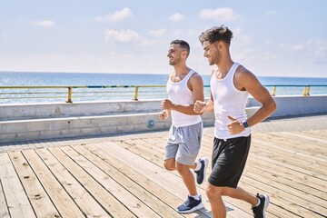 Fototapeta premium Two hispanic men sporty couple smiling confident running at seaside