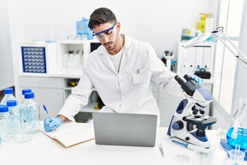 Handsome hispanic man working as scientific with microscope and laptop at laboratory