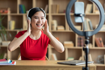 Cheerful emotional pretty millennial chinese woman blogger in wearing headphones shooting video for blog
