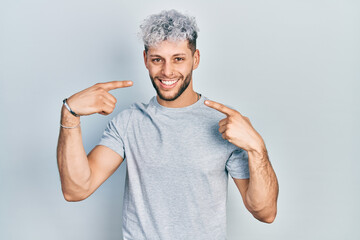 Young hispanic man with modern dyed hair wearing casual grey t shirt smiling cheerful showing and pointing with fingers teeth and mouth. dental health concept.