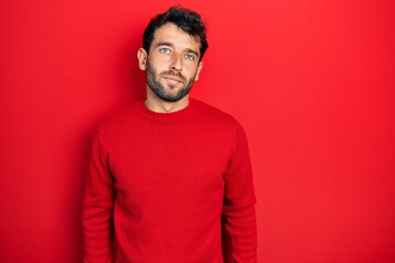 Handsome man with beard wearing casual red sweater relaxed with serious expression on face. simple and natural looking at the camera.