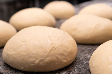 Close-up of balls of fresh raw dough for baking buns or other wheat flour products, on the kitchen table. Blank for baking