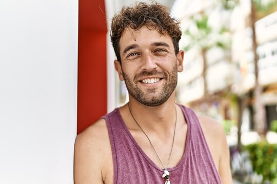 Young hispanic man smiling confident leaning on wall at street