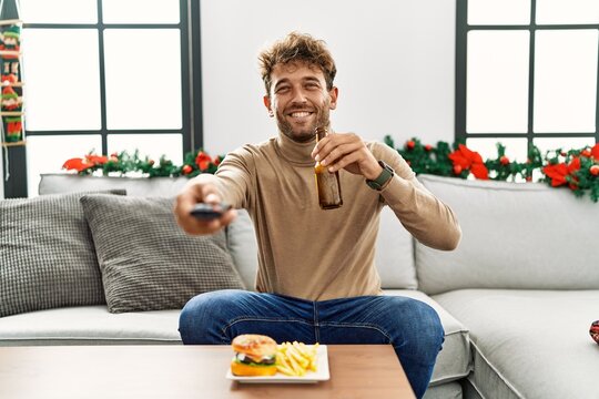 Young hispanic man watching movie sitting by christmas decor at home