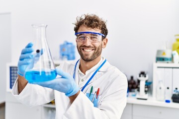 Young hispanic man wearing scientist uniform holding test tube at laboratory