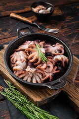 Fried baby octopuses in a skillet with herbs. Wooden background. Top view