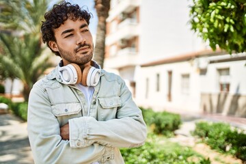 Handsome hispanic man with beard smiling happy outdoors on a sunny day wearing headphones