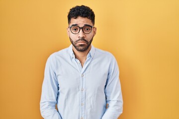 Hispanic man with beard standing over yellow background depressed and worry for distress, crying angry and afraid. sad expression.
