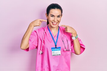 Young brunette woman wearing doctor uniform and stethoscope smiling cheerful showing and pointing...