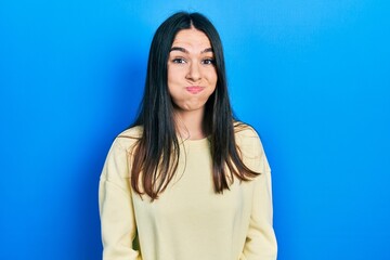 Fototapeta premium Young brunette woman wearing casual sweatshirt puffing cheeks with funny face. mouth inflated with air, crazy expression.