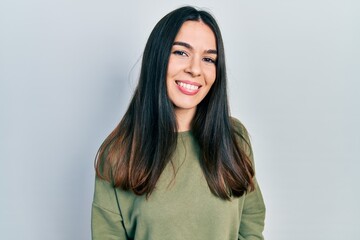 Young brunette woman wearing casual green sweater looking positive and happy standing and smiling...