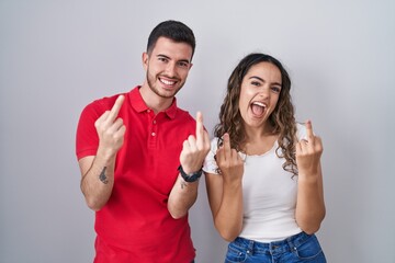 Young hispanic couple standing over isolated background showing middle finger doing fuck you bad...