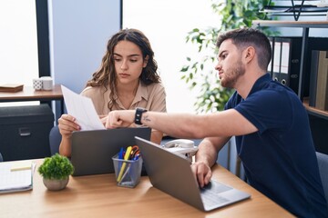 Young hispanic couple business workers using laptop reading document at office