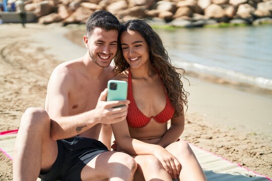 Young hispanic couple tourists wearing swimsuit make selfie by smartphone at seaside