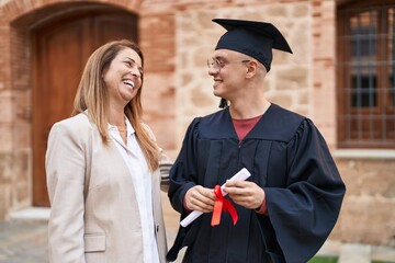 Man and woman mother and son standing together holding graduate diploma at university