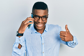 Young african american man having conversation talking on the smartphone smiling happy and positive, thumb up doing excellent and approval sign