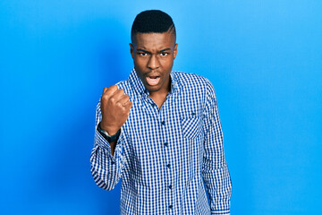 Young african american man wearing casual clothes angry and mad raising fist frustrated and furious...