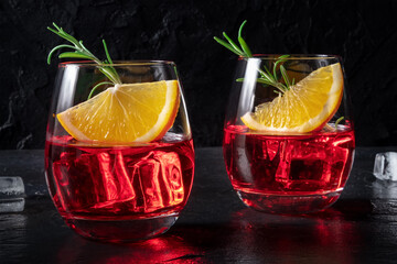 Negroni aperitif cocktail with campari, aperol and fresh oranges and rosemary, a cold drink, on a black background