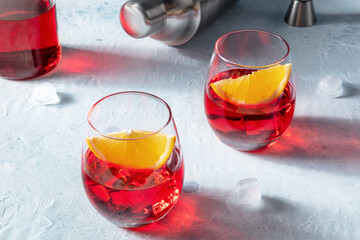 Campari orange cocktails with a jigger and a shaker, with ice cubes and a bottle in the background, on a slate table