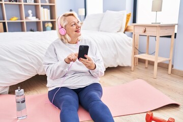 Middle age blonde woman smiling confident listening to music at bedroom