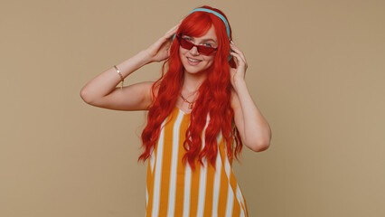 Portrait of redhead woman in tank top listening music via headphones and dancing disco fooling...