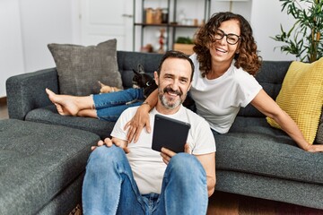 Middle age hispanic couple smiling happy and using touchpad. Sitting on the sofa with dogs at home.